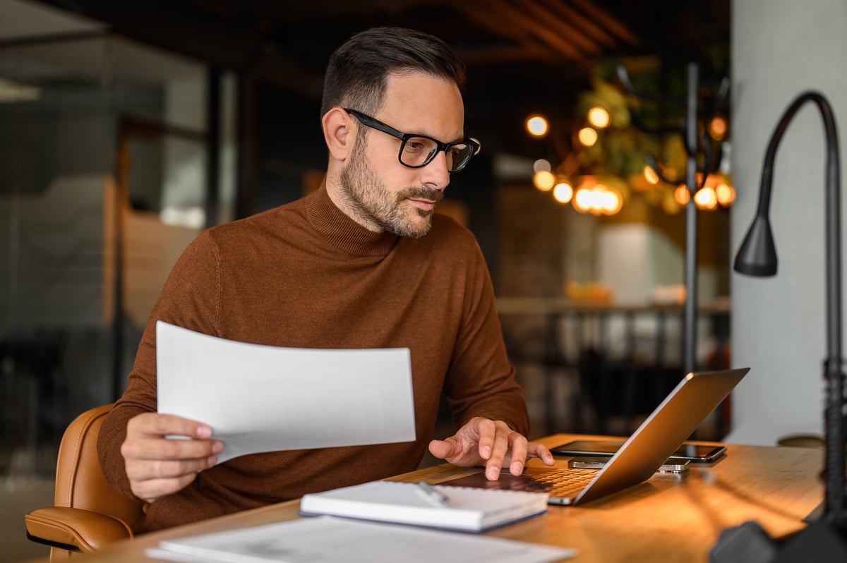 Focused business manager auditing financial report and using laptop on desk in office