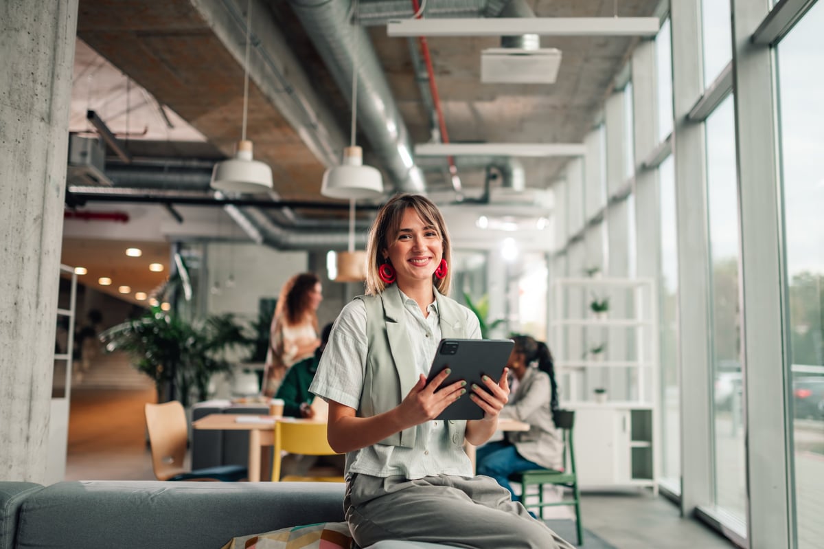Smiling businesswoman sitting in a contemporary coworking space, working with a digital tablet and looking at camera